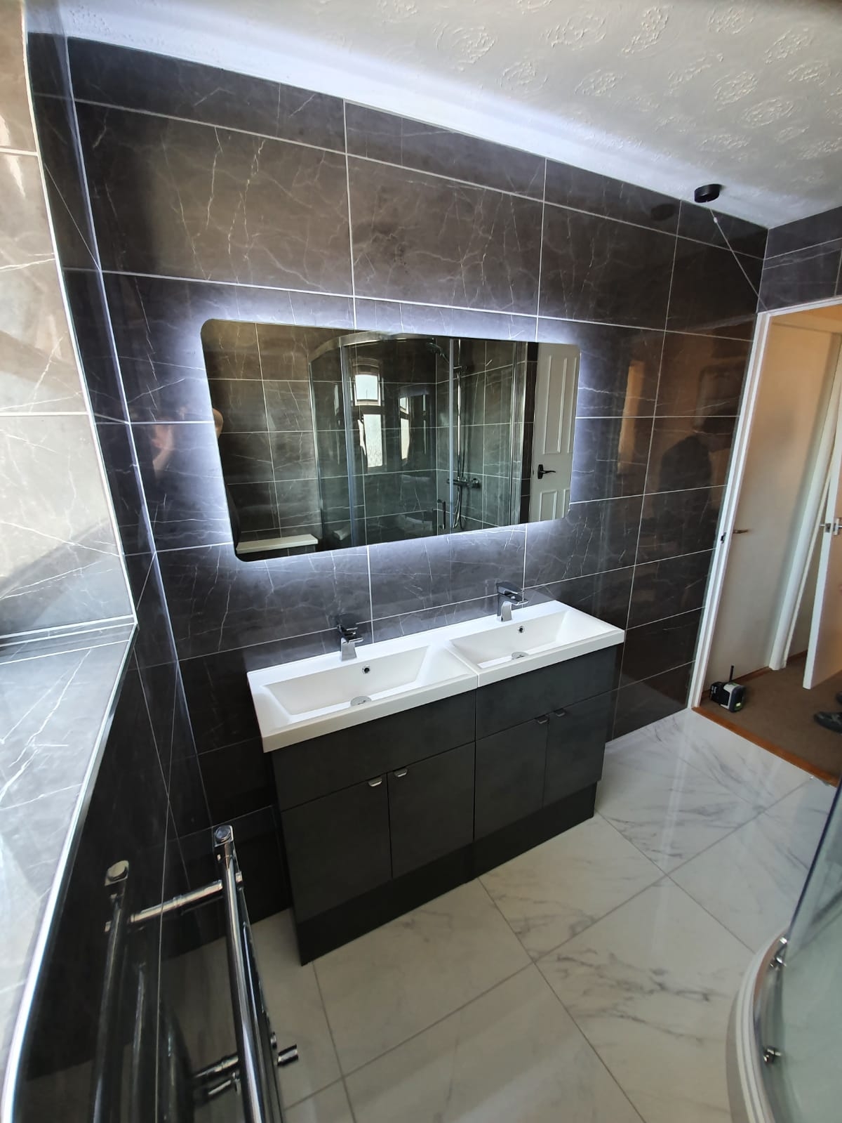 Dark tiled bathroom with a double vanity unit and a backlit mirror