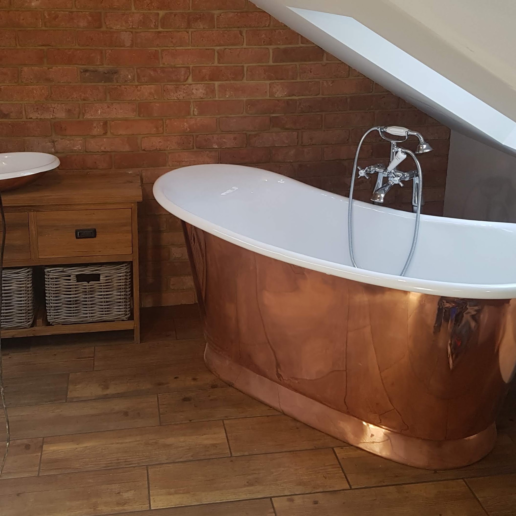 Copper roll-top bath in a loft bathroom with a brick wall and wood-effect floor