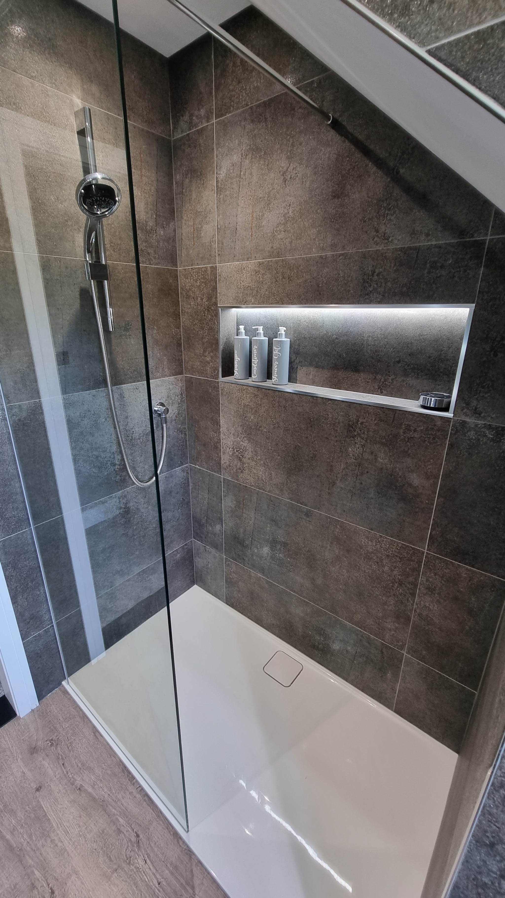 Walk-in shower with brown stone-effect tiles and a lit shelf niche