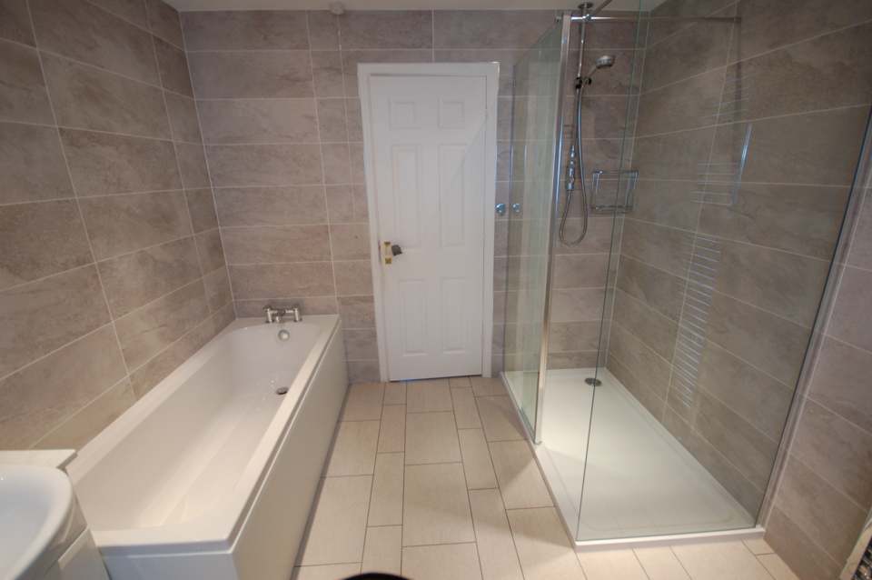 Bath and separate walk-in shower in a stone-tiled bathroom