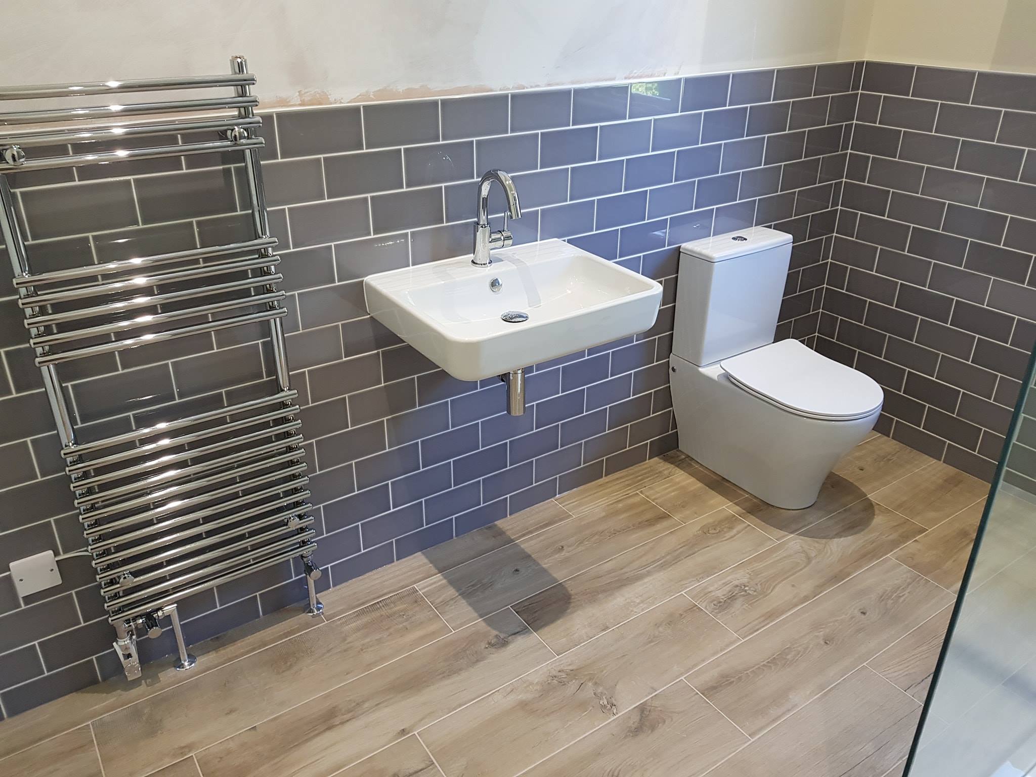 Wall-hung basin, towel rail and wood-effect floor in an ensuite